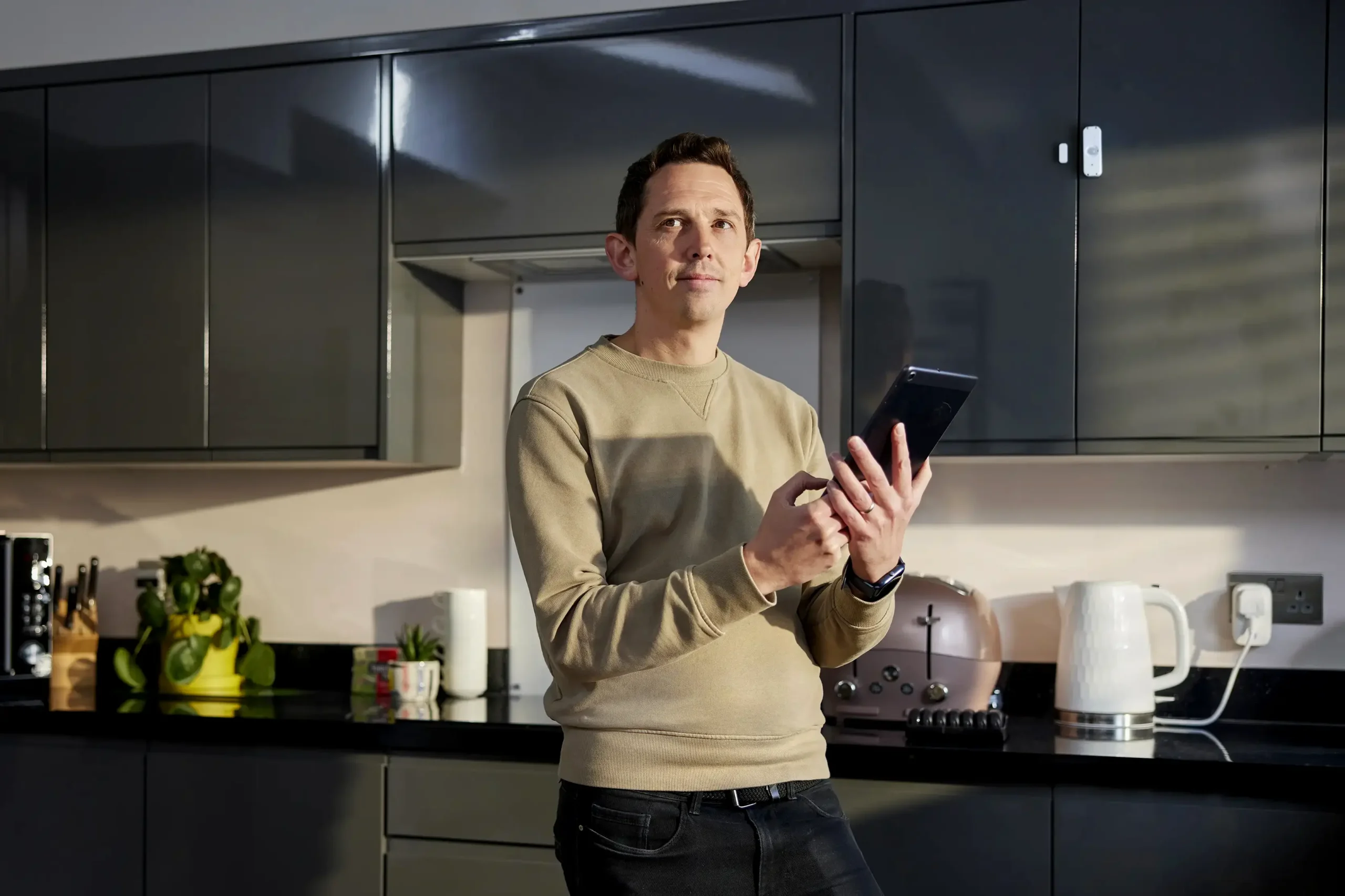 Man standing in the kitchen holding a tablet, using Canary Care's remote monitoring tech to care for a loved one from afar.